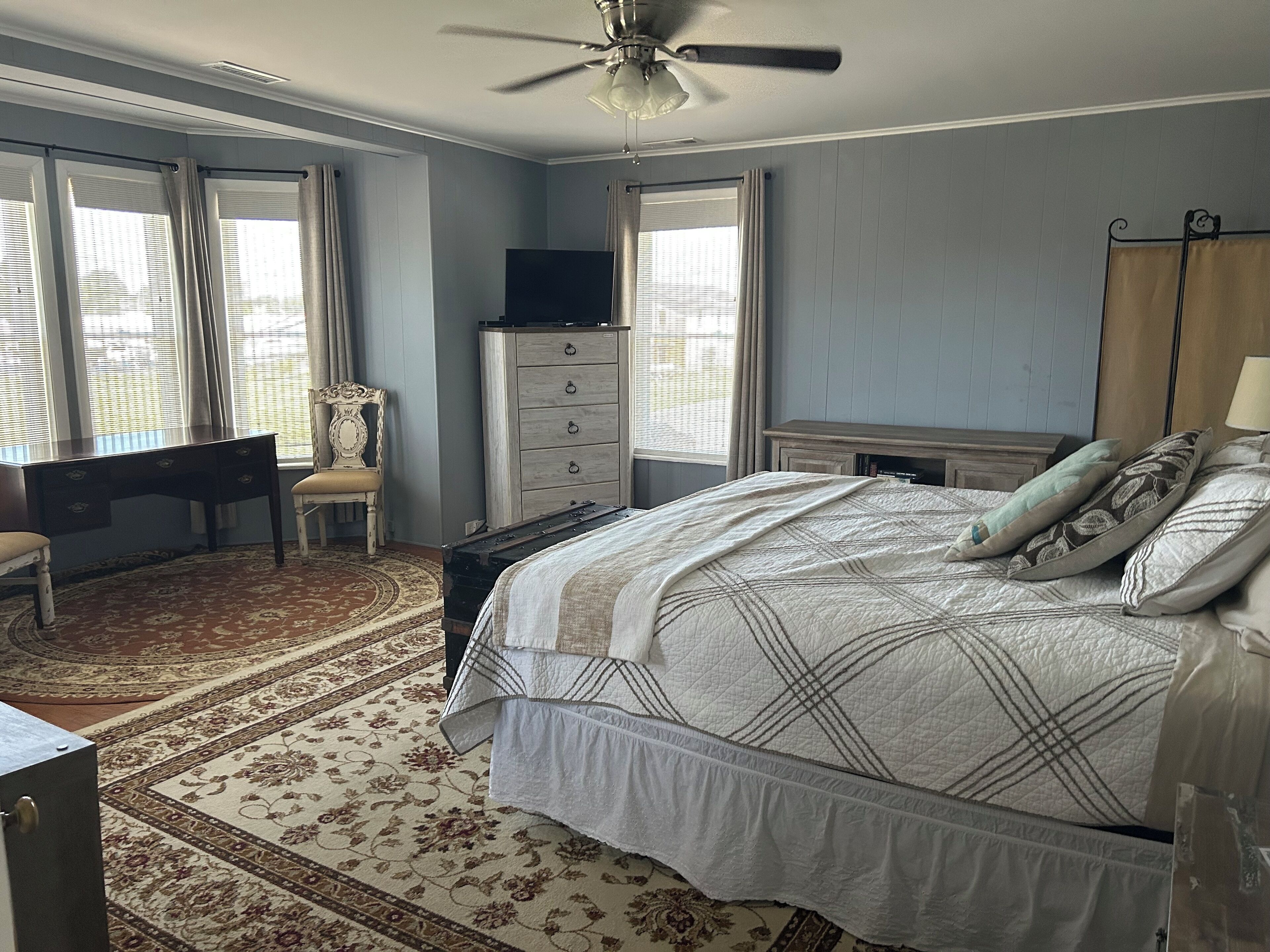 A bedroom with a bed, a desk, a chair, a dresser, a television, and a ceiling fan.