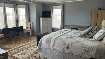 A bedroom with a bed, a desk, a chair, a dresser, a television, and a ceiling fan.