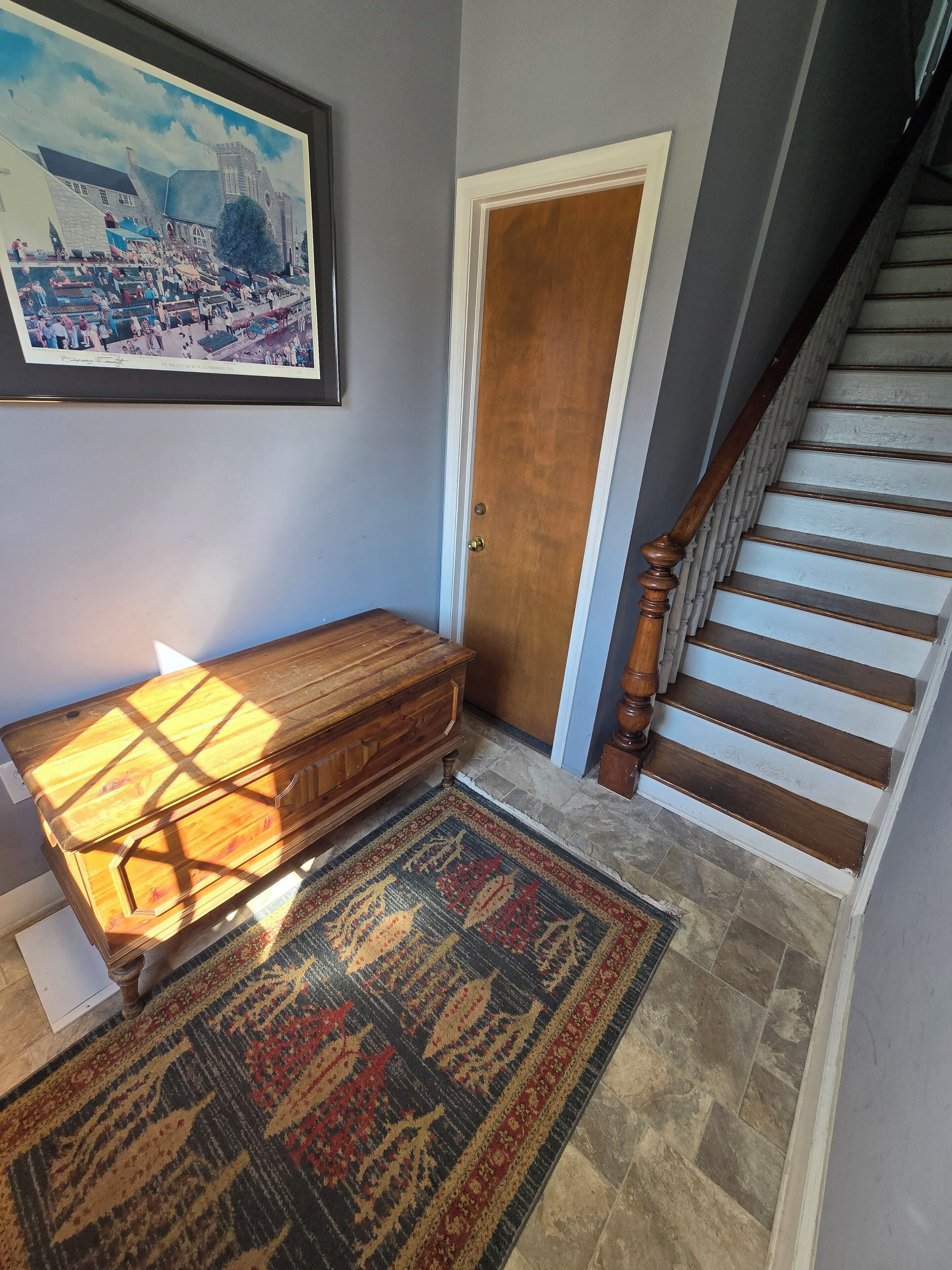 Un couloir avec un banc en bois, un tapis à motifs, une porte et un escalier.