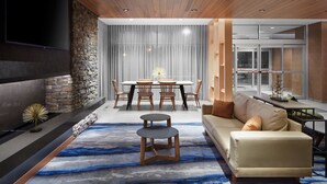A modern living room with a stone accent wall, a flat-screen TV, a dining area with a table and chairs, and a sofa with cushions. - Fairfield Inn & Suites by Marriott Middletown (Middletown)