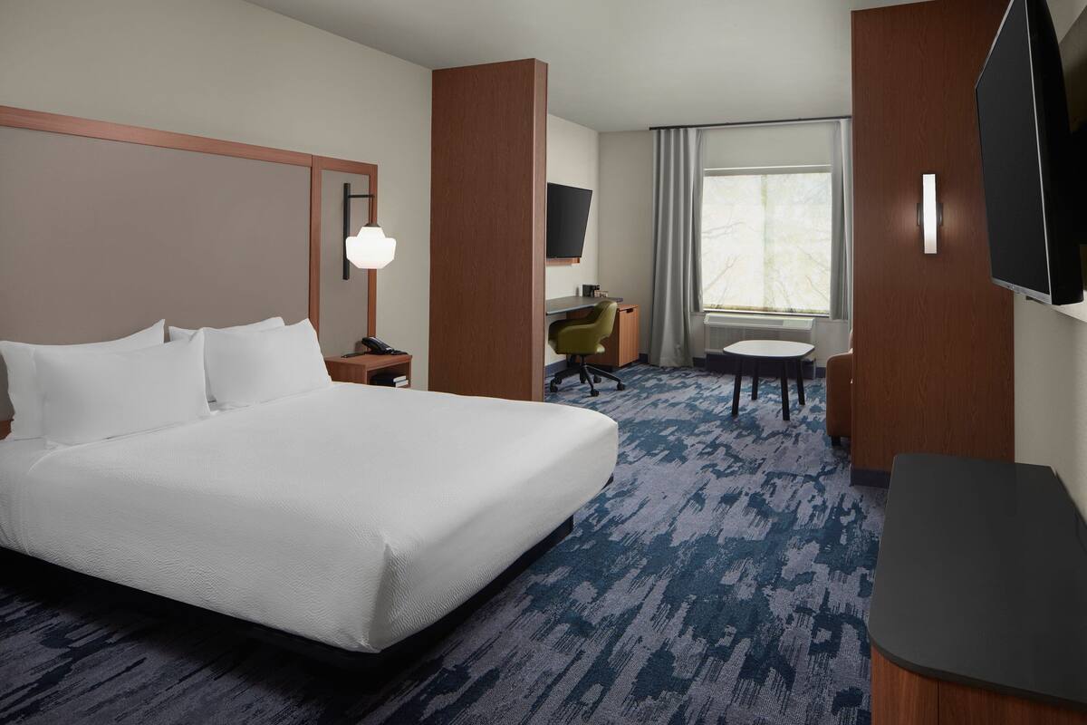 A hotel room with a large bed, a desk, a chair, a television, and a window with curtains.