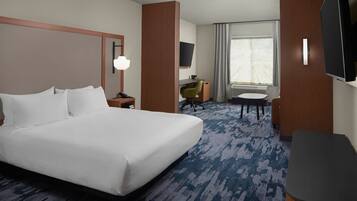 A hotel room with a large bed, a desk, a chair, a television, and a window with curtains.