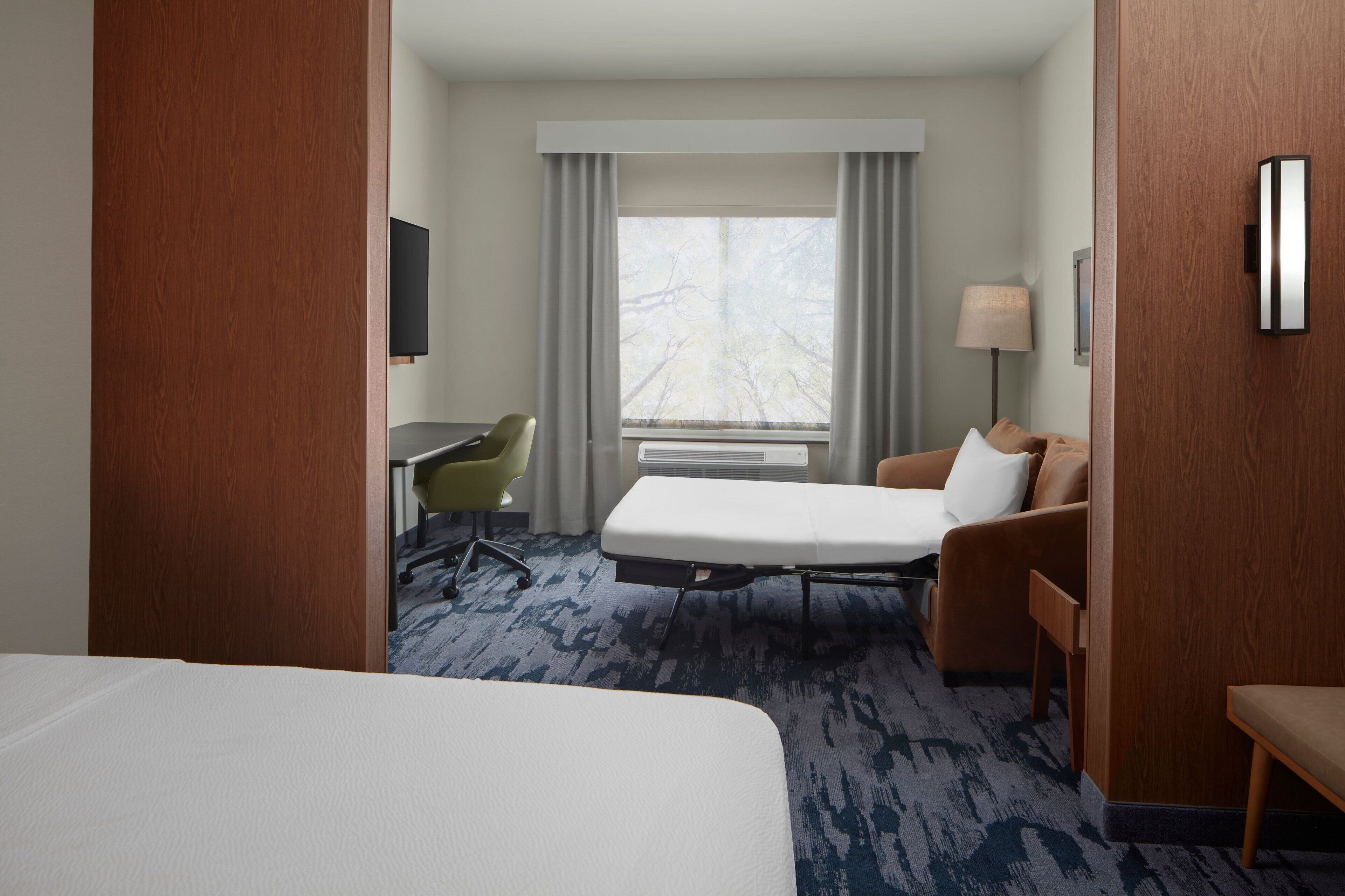 Habitación de hotel con cama, escritorio, silla, sofá y ventana con cortinas.