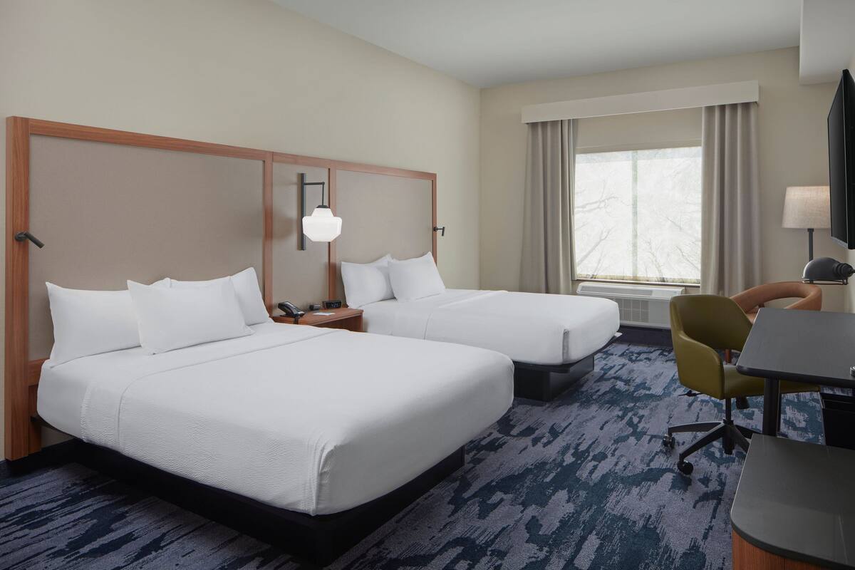 A hotel room with two beds, a desk, a chair, a TV, and a window with curtains.