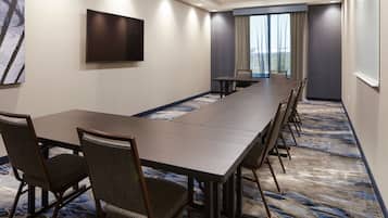 A conference room with a long table, chairs, a flat-screen TV, and a large window with curtains.