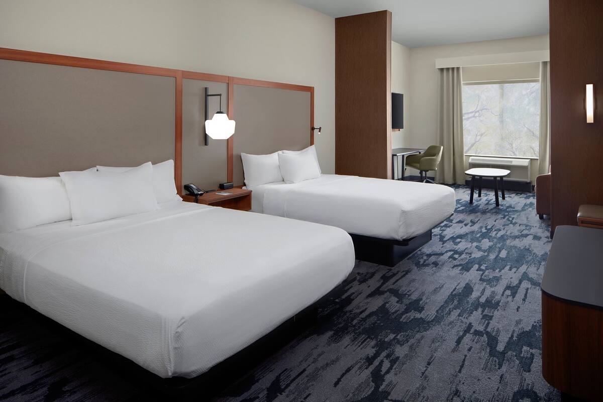 A hotel room with two beds, a desk, a chair, and a small table.