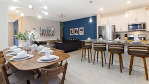 Una cocina moderna con armarios blancos, electrodomésticos de acero inoxidable y una zona de comedor con mesa de madera para seis comensales.