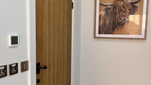 Un pasillo con una puerta de madera, un termostato y un cuadro de un toro en la pared.