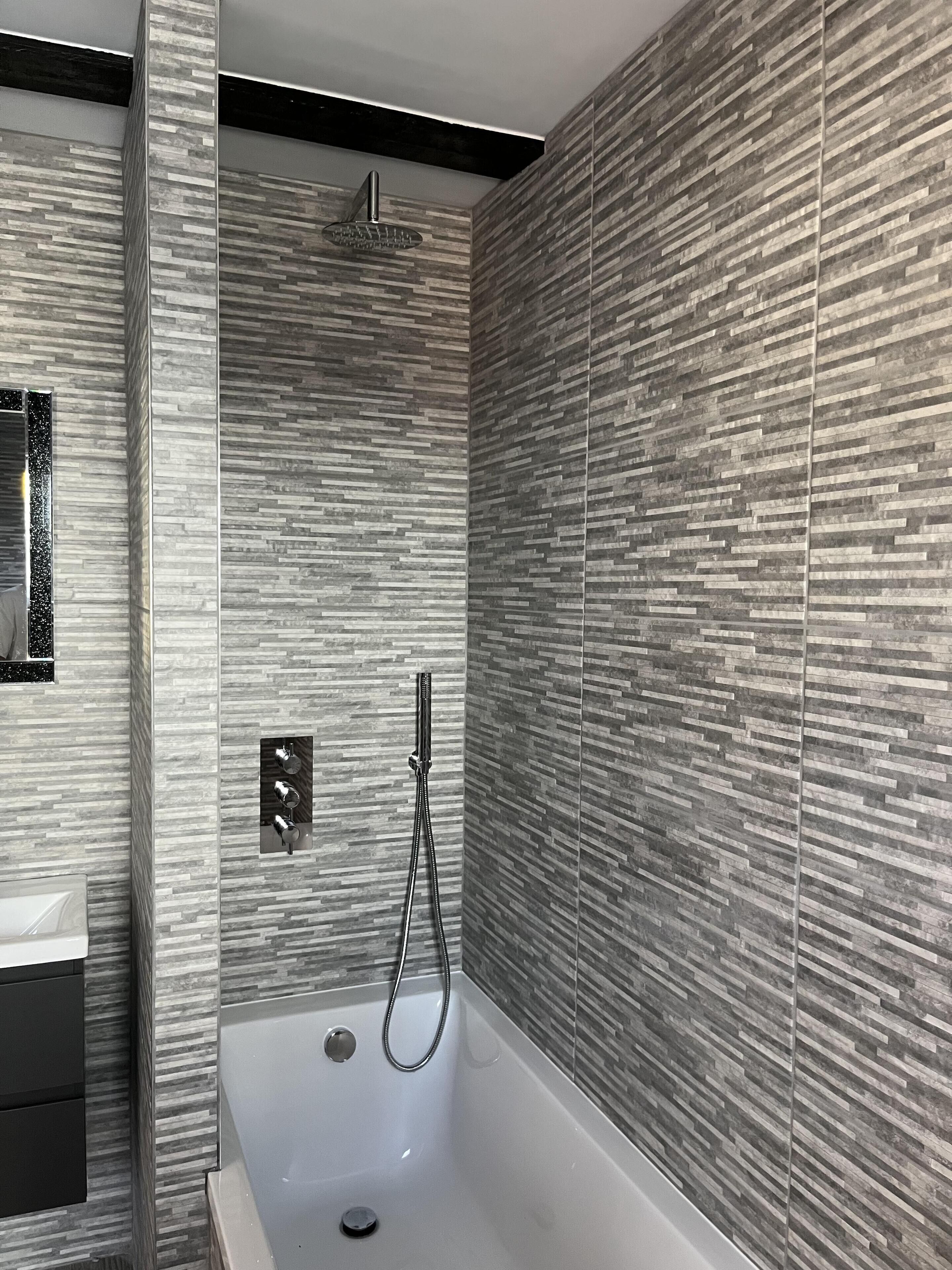 Ein modernes Badezimmer mit freistehender Badewanne, einer Handbrause und einem am Wand montierten Wasserhahn.