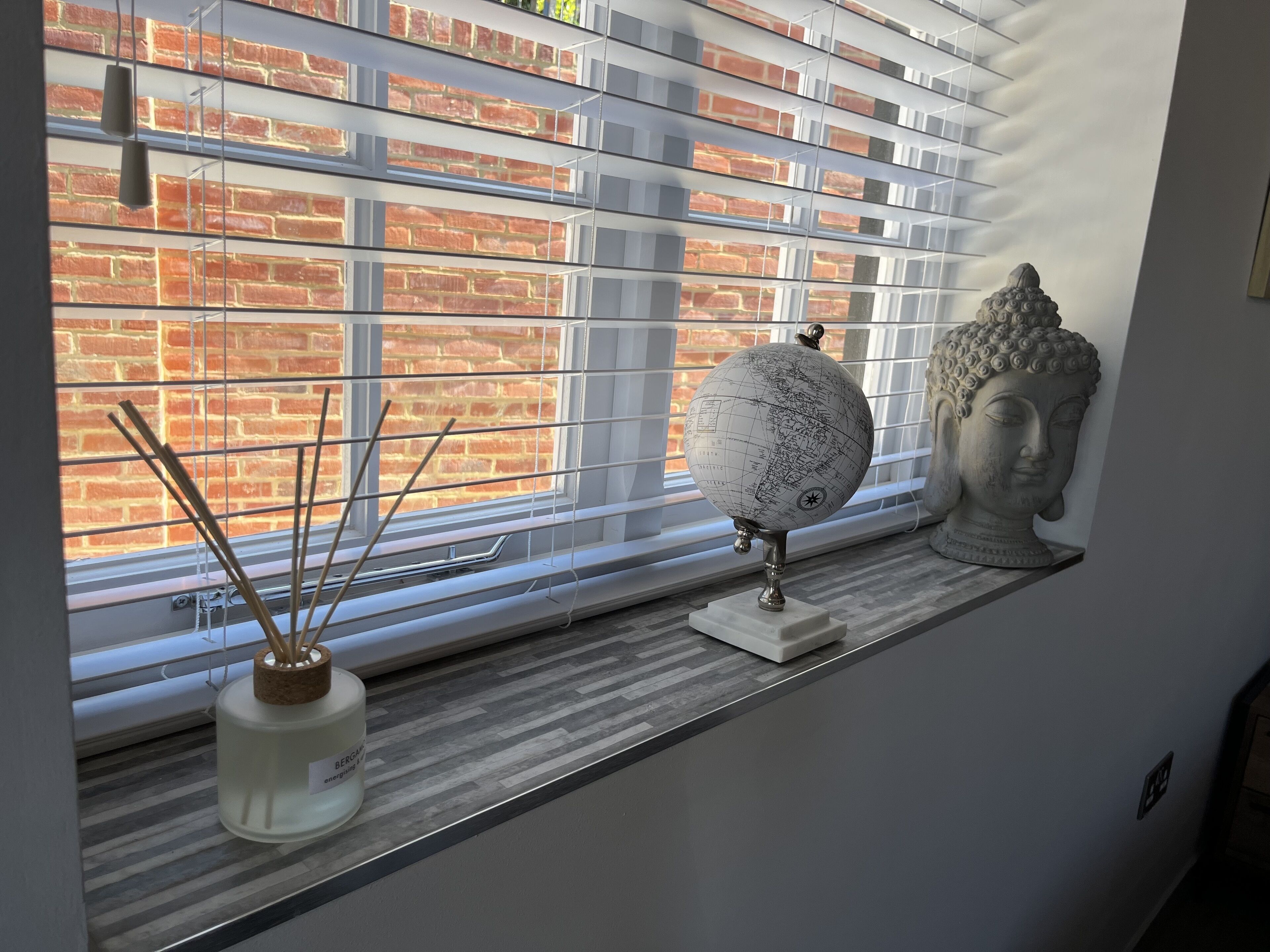 A window with a view of a brick wall, a globe, and a Buddha statue on a shelf.
