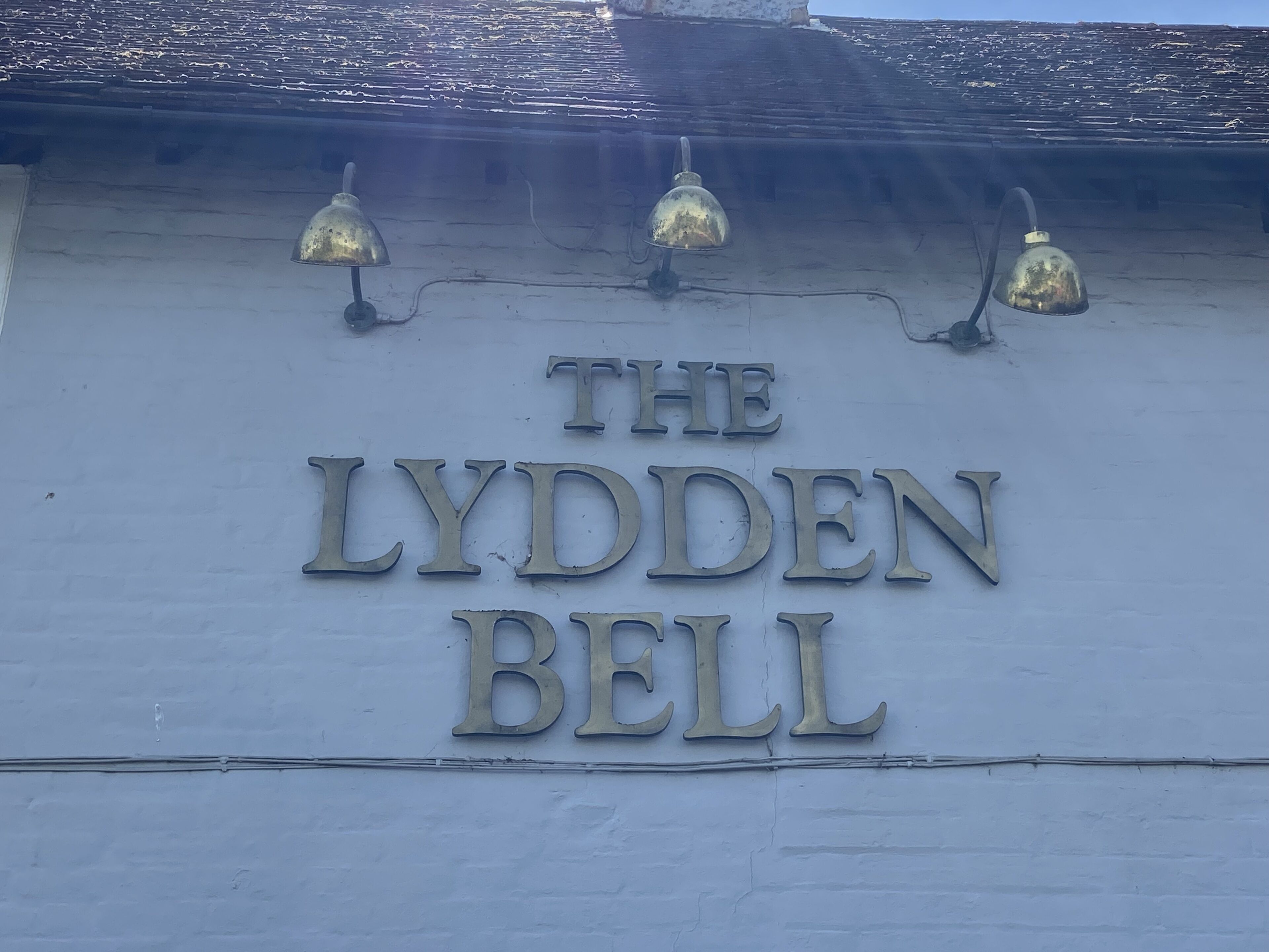 Un letrero que dice 'THE LYDDEN BELL' con tres lámparas encima.