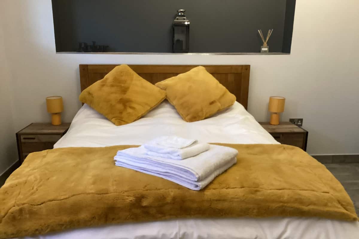 Ein ordentlich gemachtes Bett mit einer braunen Decke, zwei Kissen, einem gefalteten weißen Handtuch und zwei Nachttischlampen auf Holznachttischen.