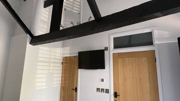 Een kamer met witte wanden, een houten deur, een tv aan de muur en een plafond met zichtbare balken.