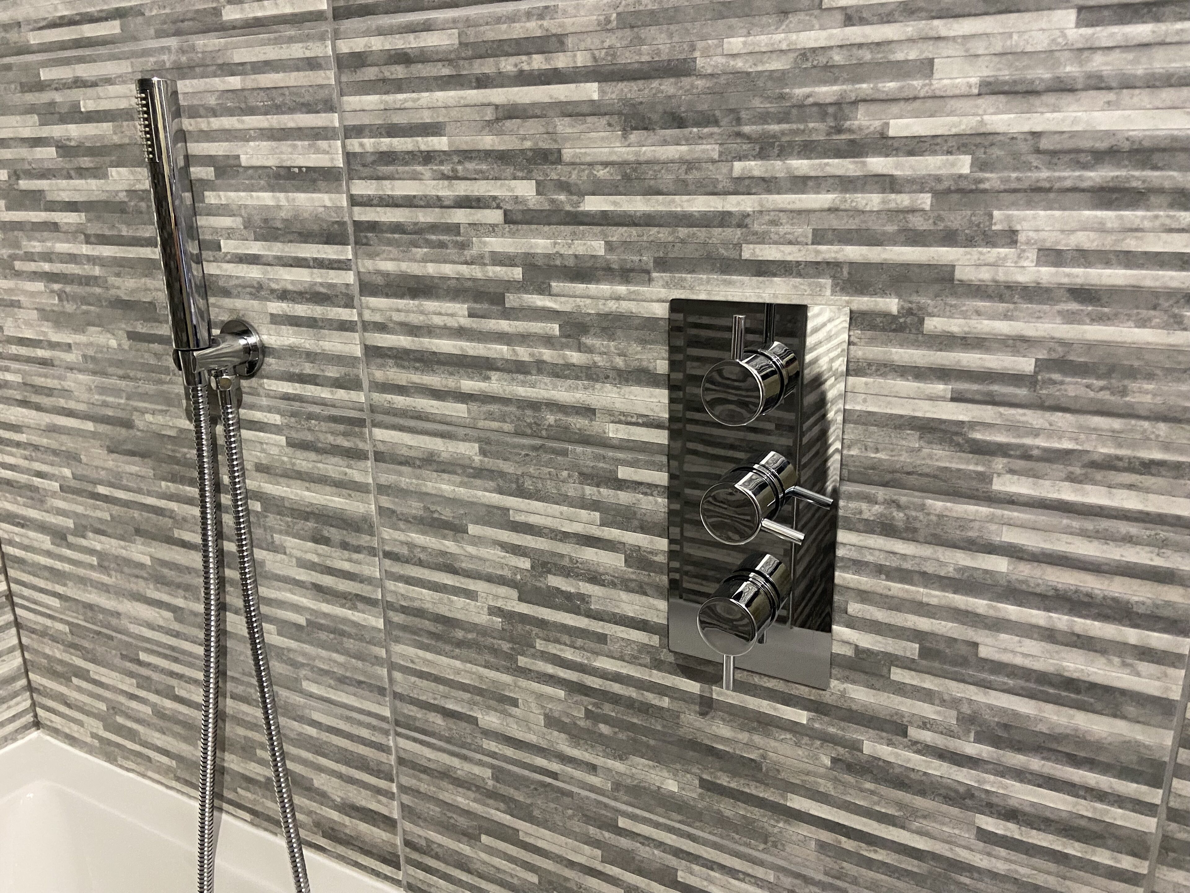 Un espacio de ducha con diseño moderno, que presenta una pared texturizada y un cabezal de ducha empotrado con múltiples rociadores.
