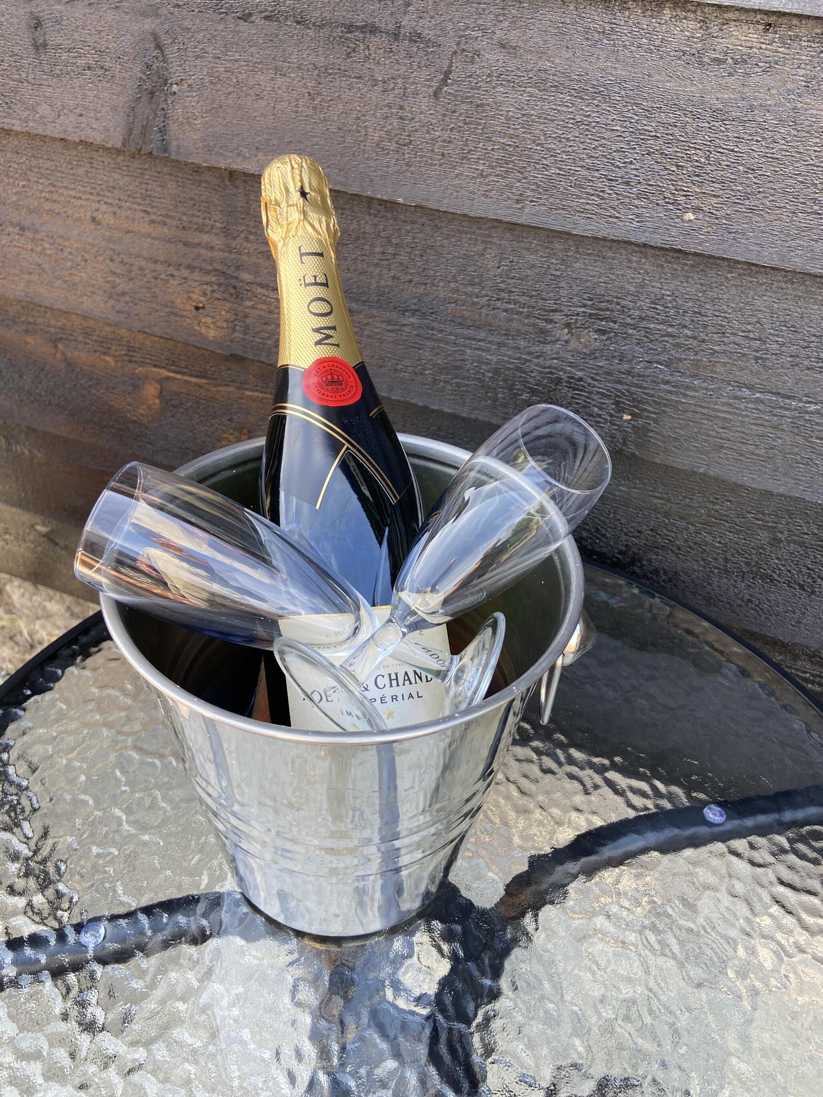A bottle of champagne in a metal bucket with glasses.