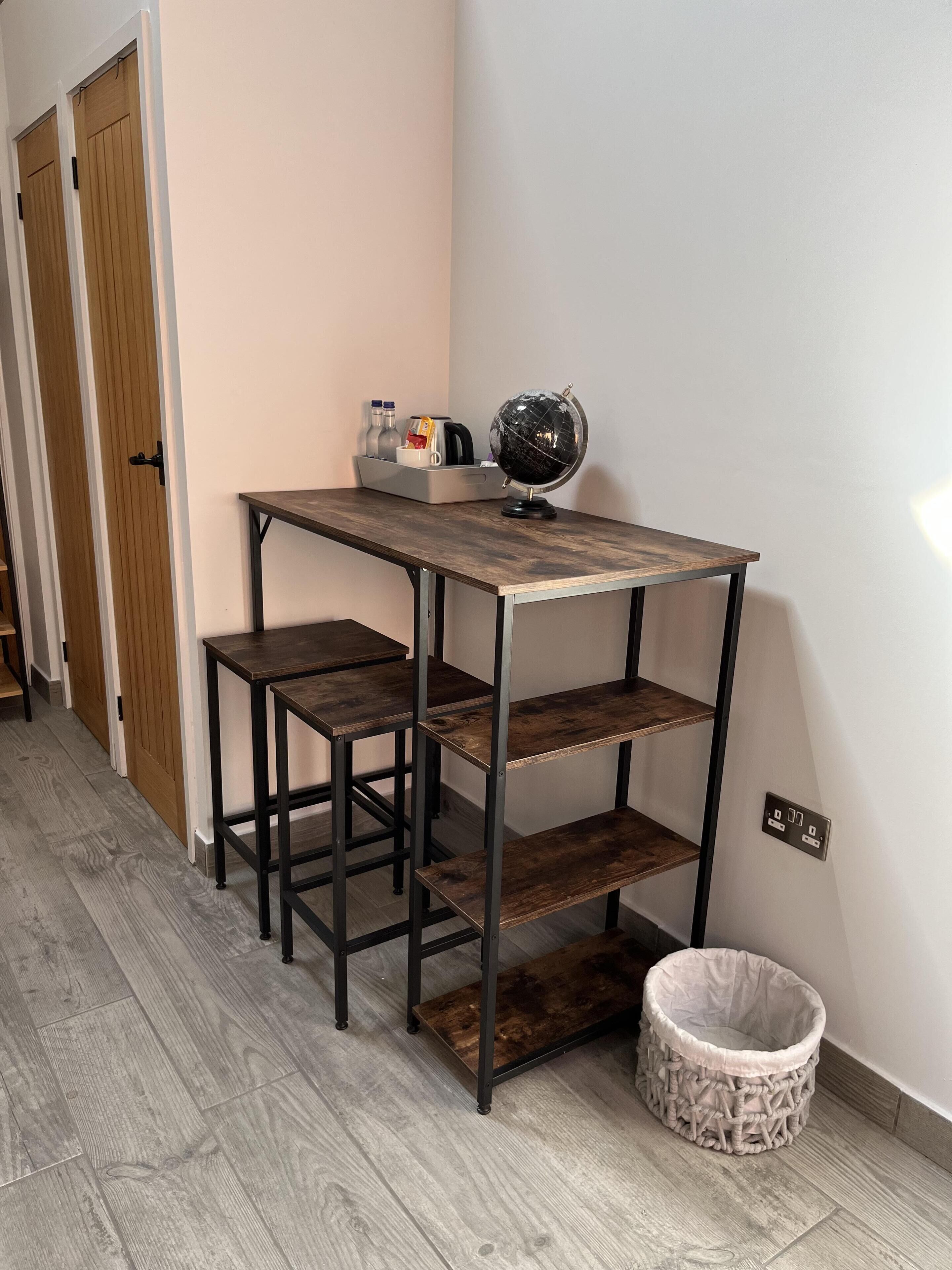 A small, rustic kitchenette with a wooden table, two stools, and a globe on the table.