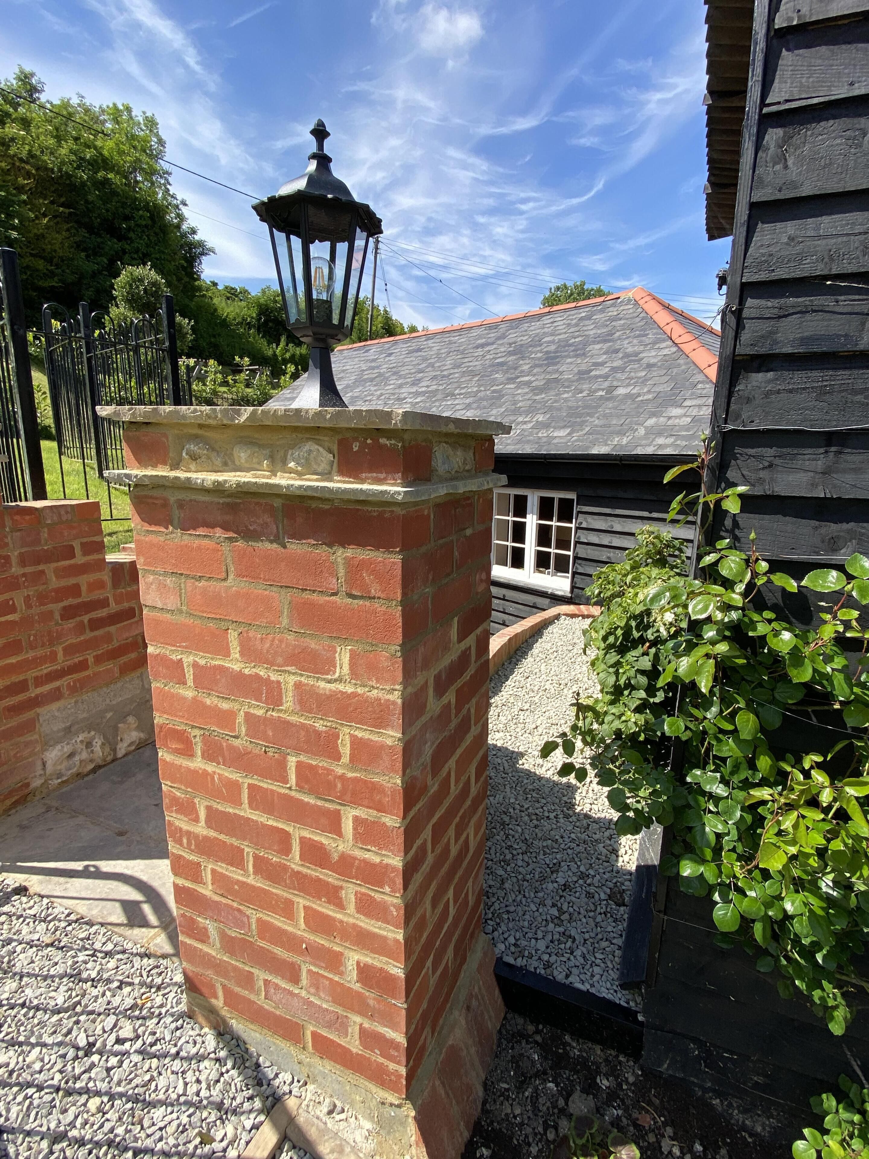 A brick pillar with a lantern, a wooden house with a tiled roof, and a gravel path.