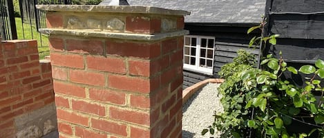 A brick pillar with a lantern, a wooden house with a tiled roof, and a gravel path.
