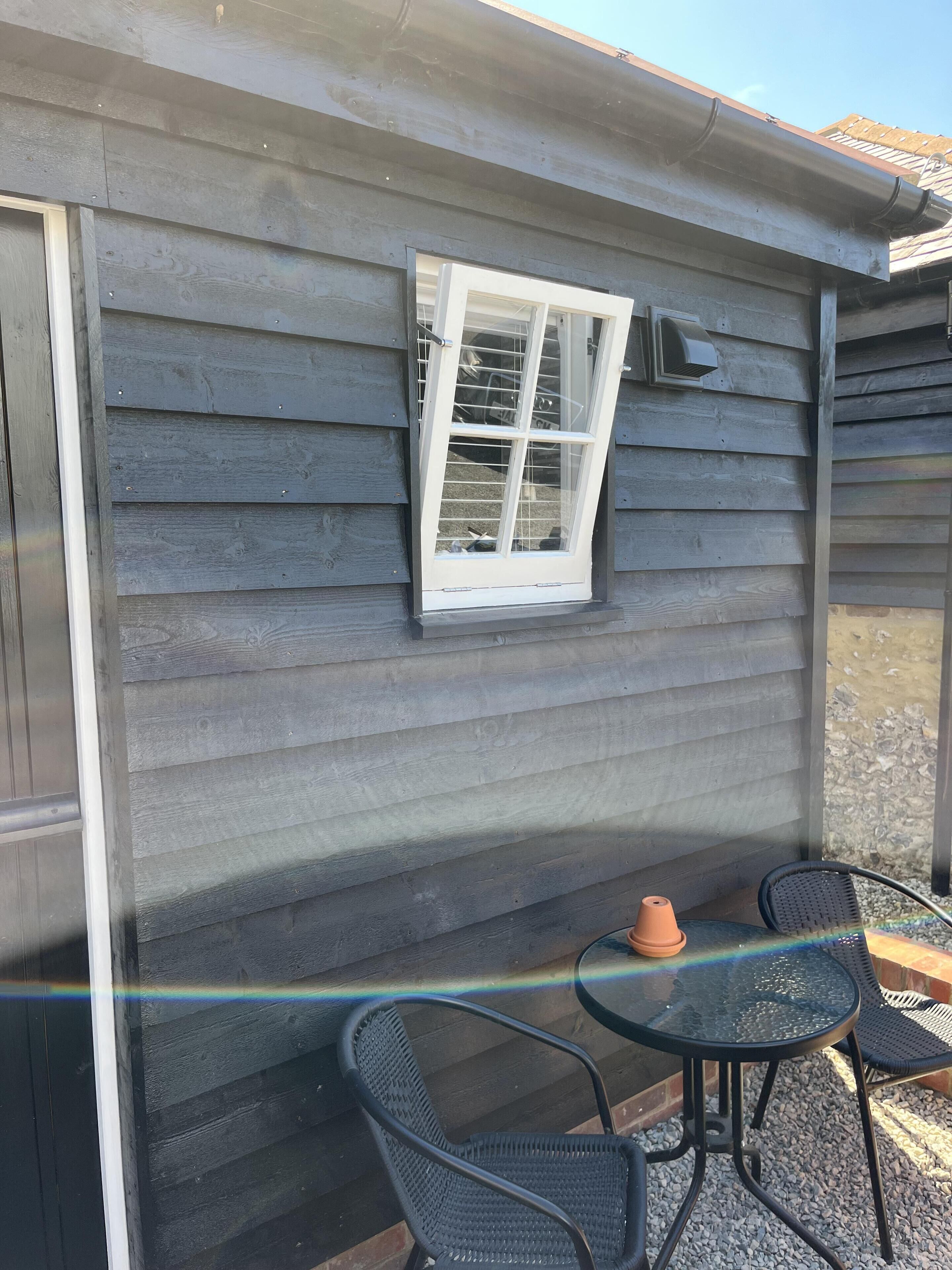 Un patio techado con una mesa, sillas, una ventana y una pequeña mesa con una maceta de barro.
