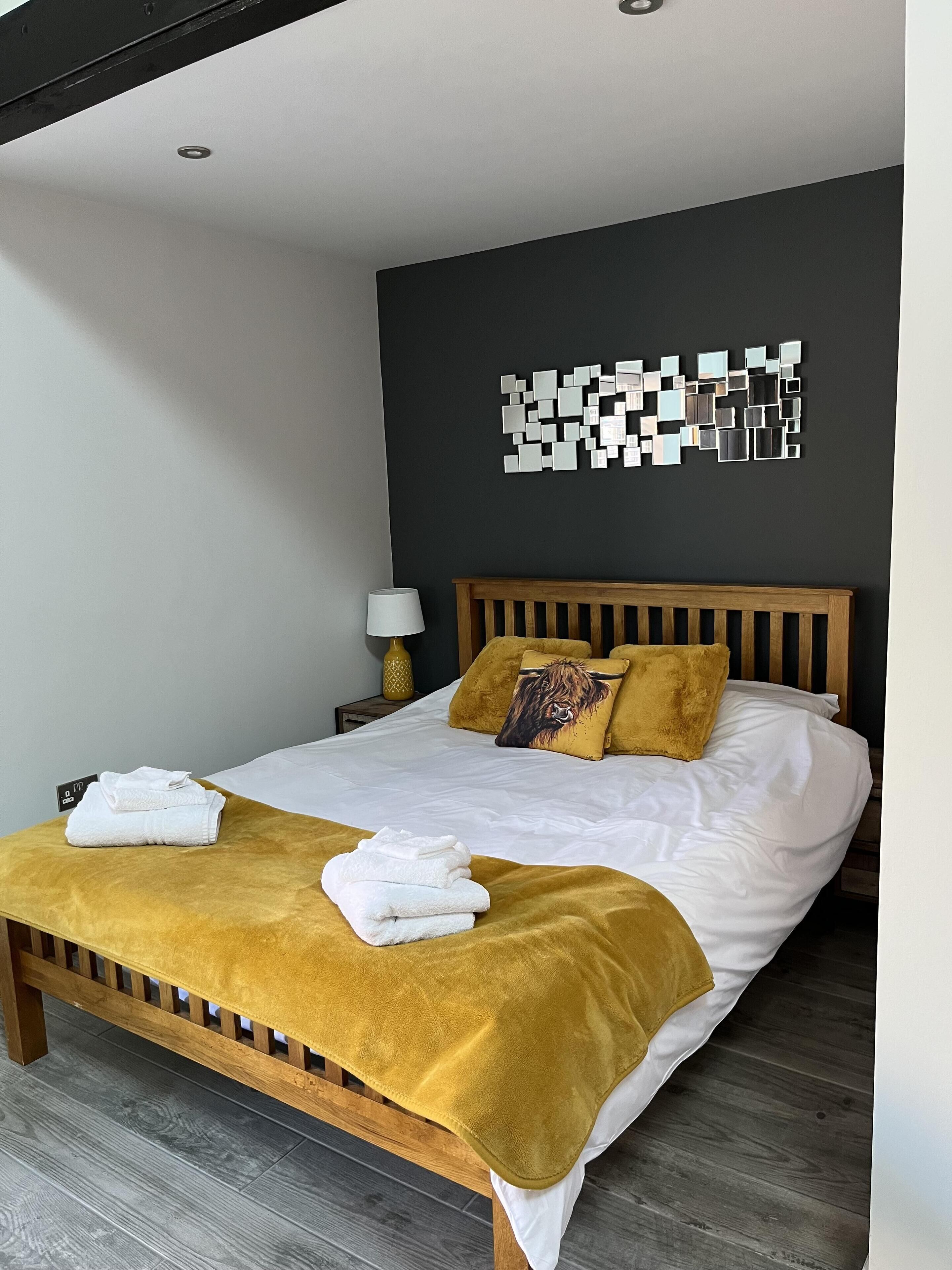 A neatly made bed with a wooden headboard, a mustard-colored throw blanket, and two pillows, one with a lion design.