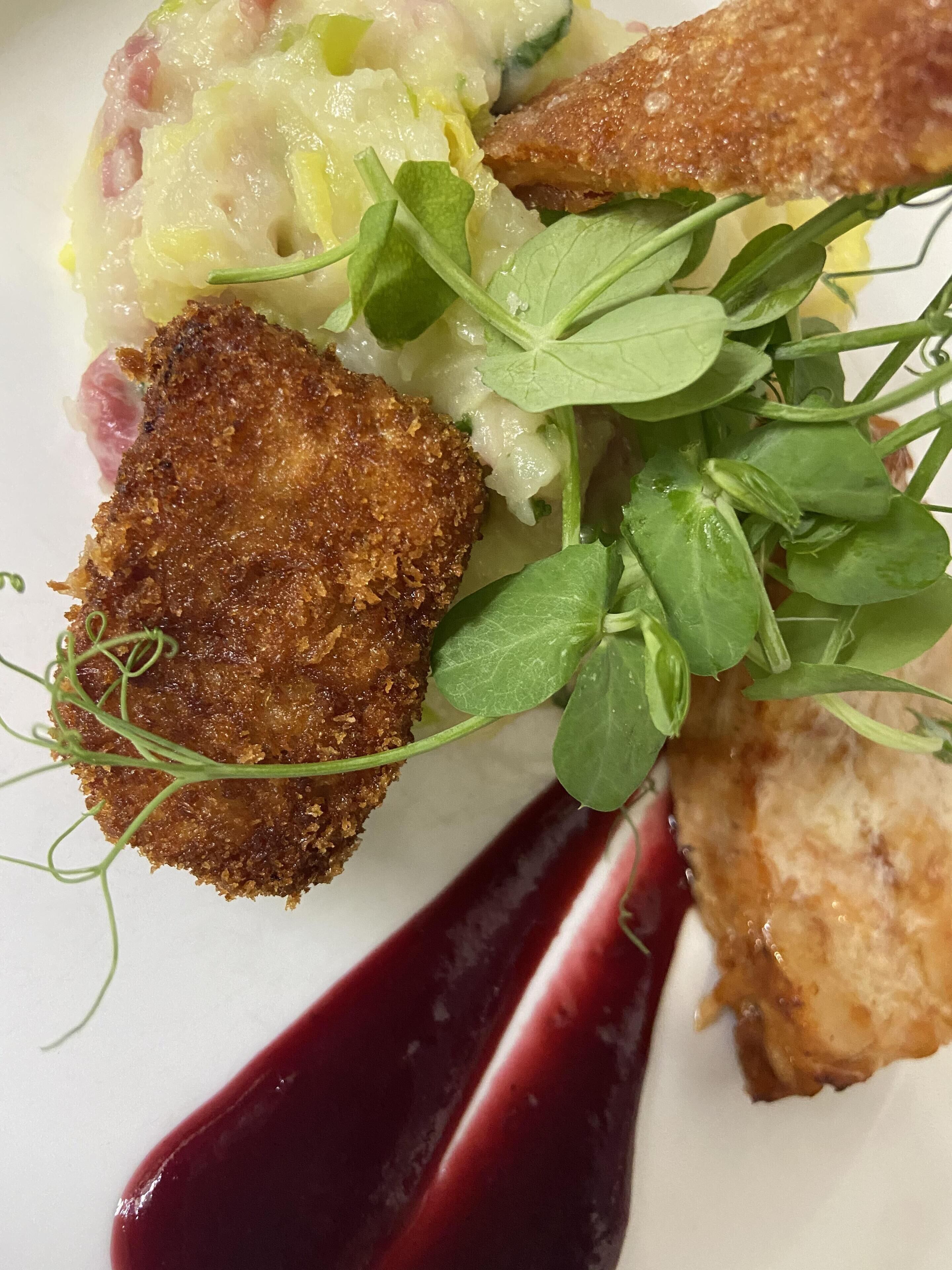 A plated dish with breaded items, a creamy side, and a dark sauce.