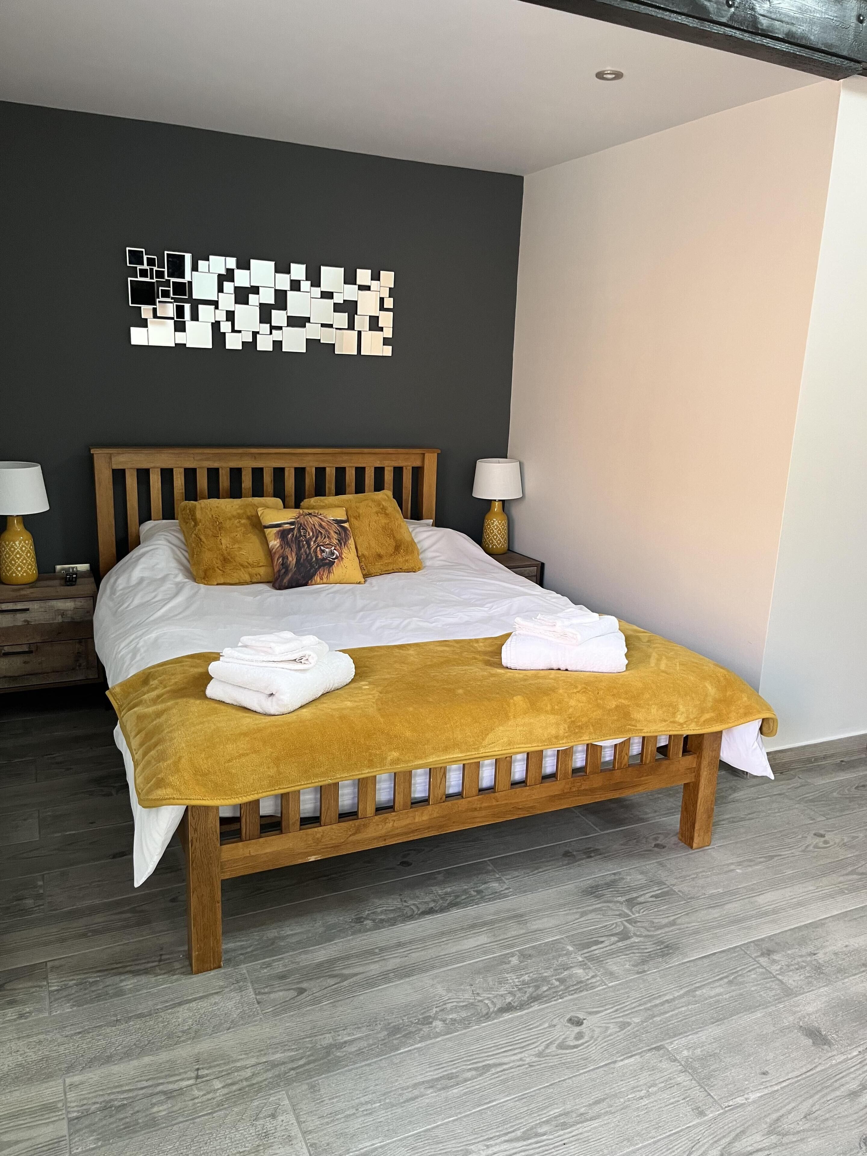 A neatly made bed with a wooden headboard, two bedside lamps, a wall art piece, and a wooden bench with towels.