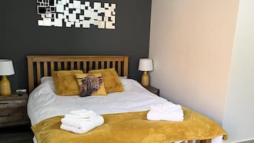 A neatly made bed with a wooden headboard, two bedside lamps, a wall art piece, and a wooden bench with towels.