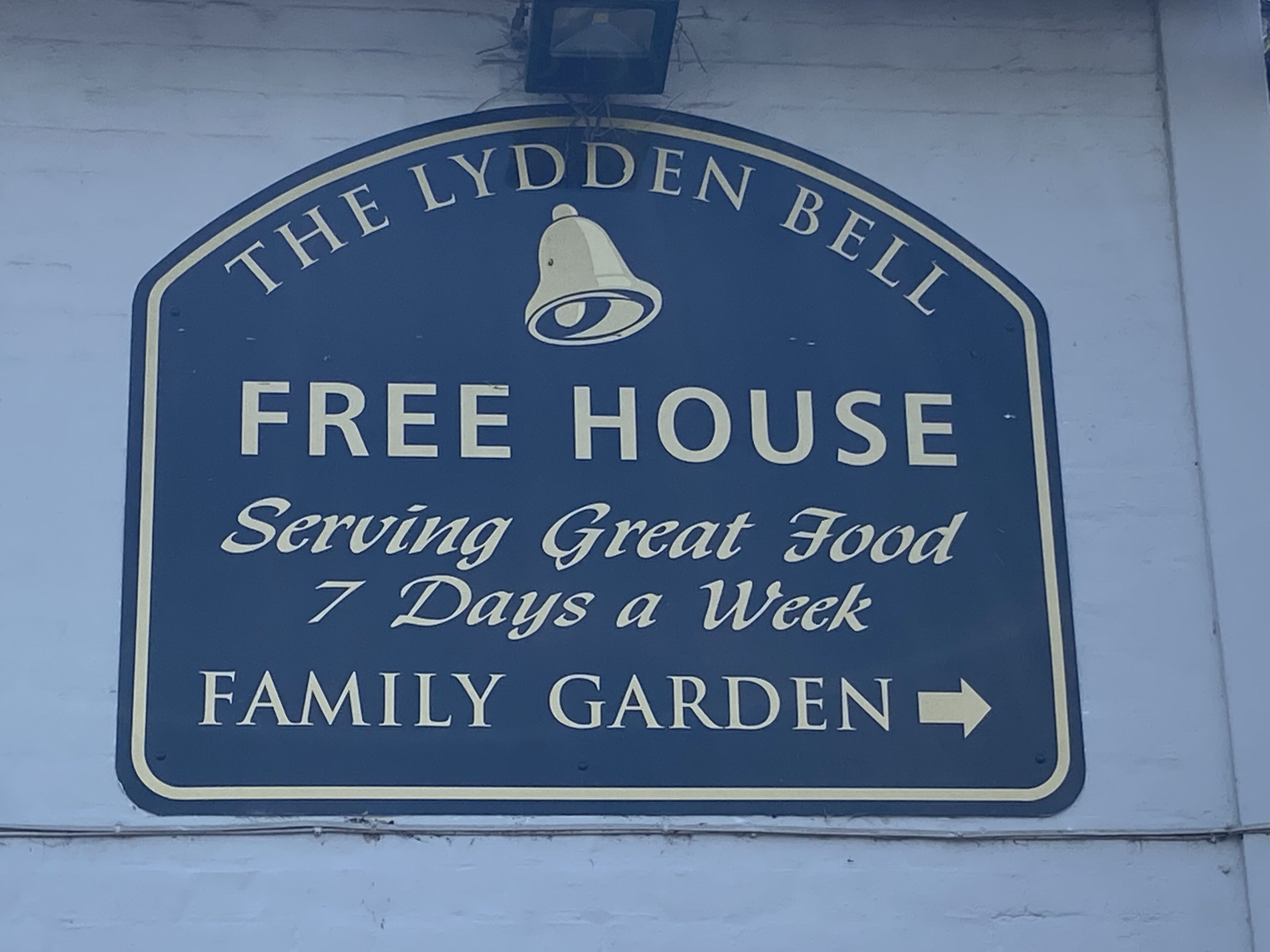 A sign for "The Llyden Bell Free House" indicating it serves great food 7 days a week and is a family garden.