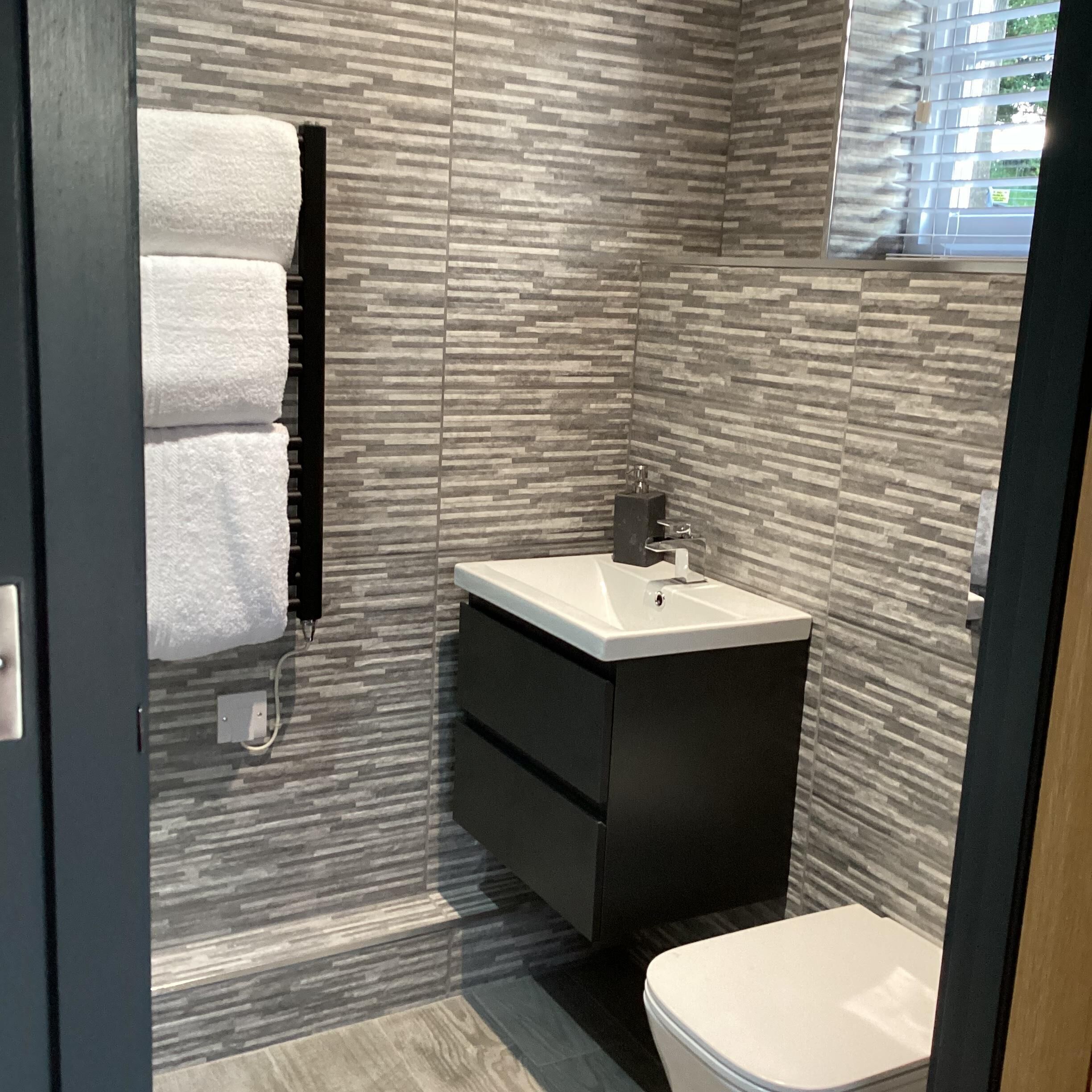 Ein modernes Badezimmer mit Fliesen, einem Waschbecken, einer Toilette und einem Handtuchhalter.