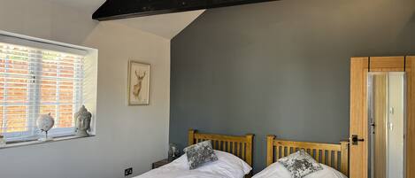 A bedroom with two beds, a window with blinds, a Buddha statue, a deer painting, and a wooden wardrobe.