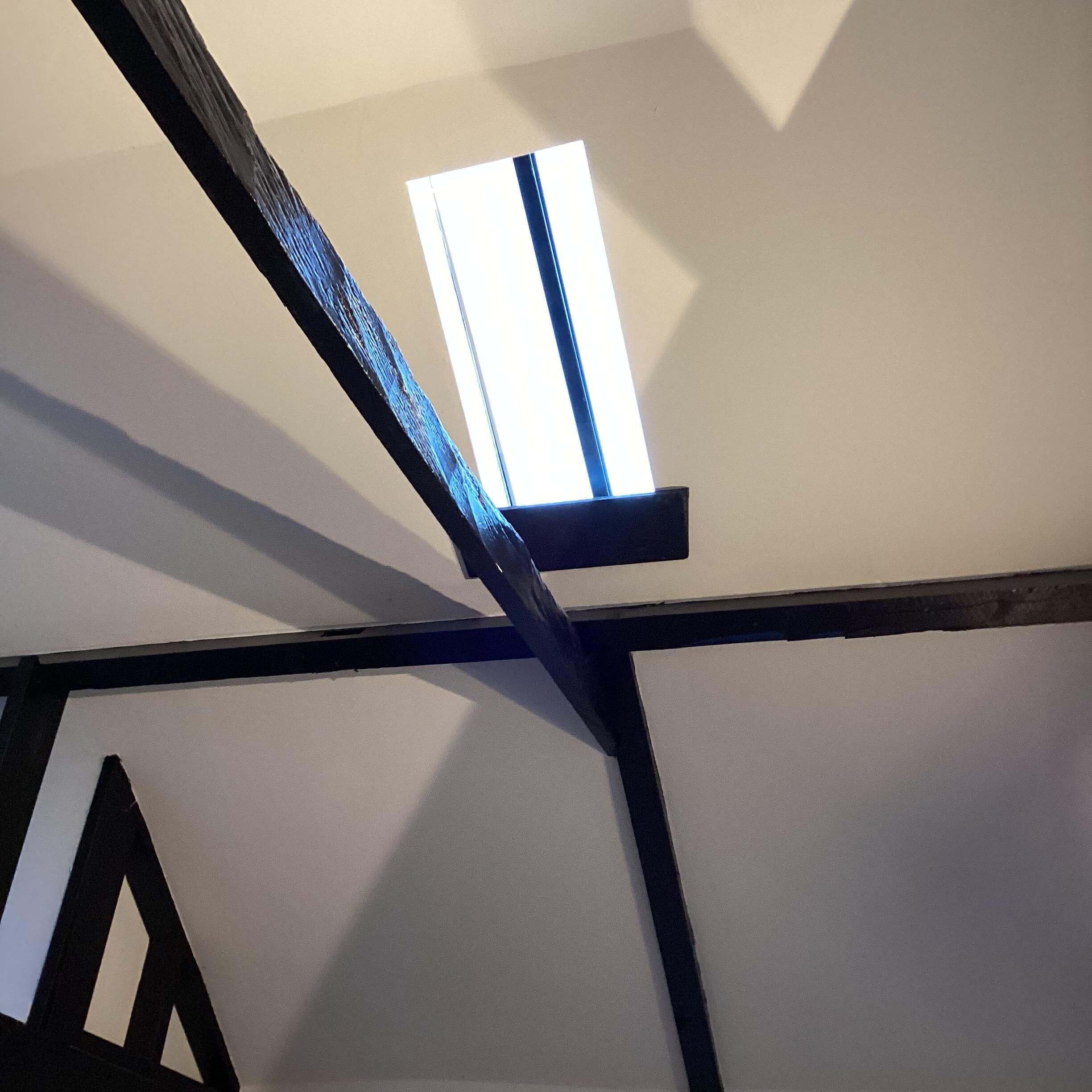 Una habitación con vigas de madera a la vista y un ventanal con persiana blanca.