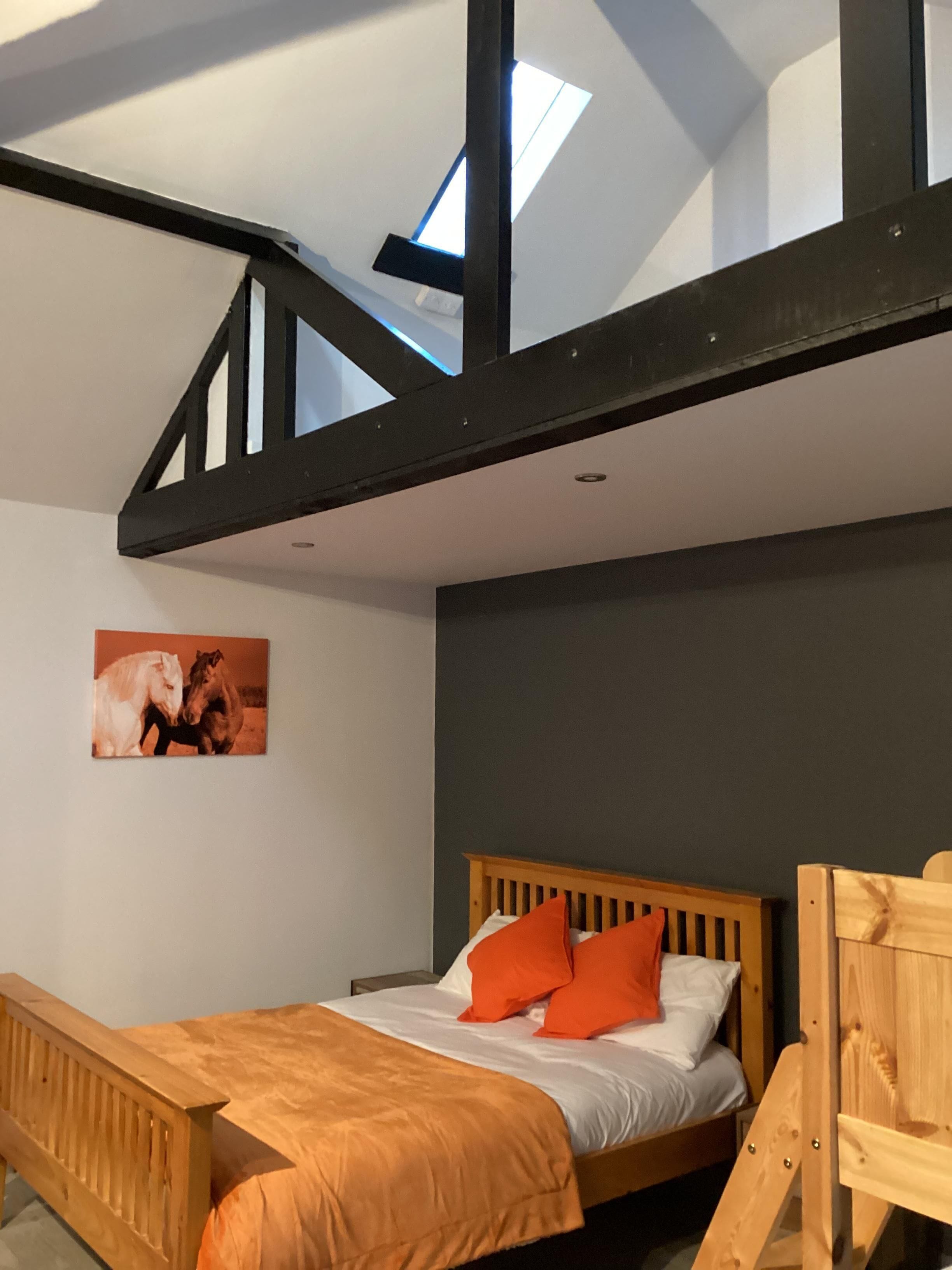 A bedroom with a wooden bed, orange bedding, a skylight, and a picture of horses on the wall.