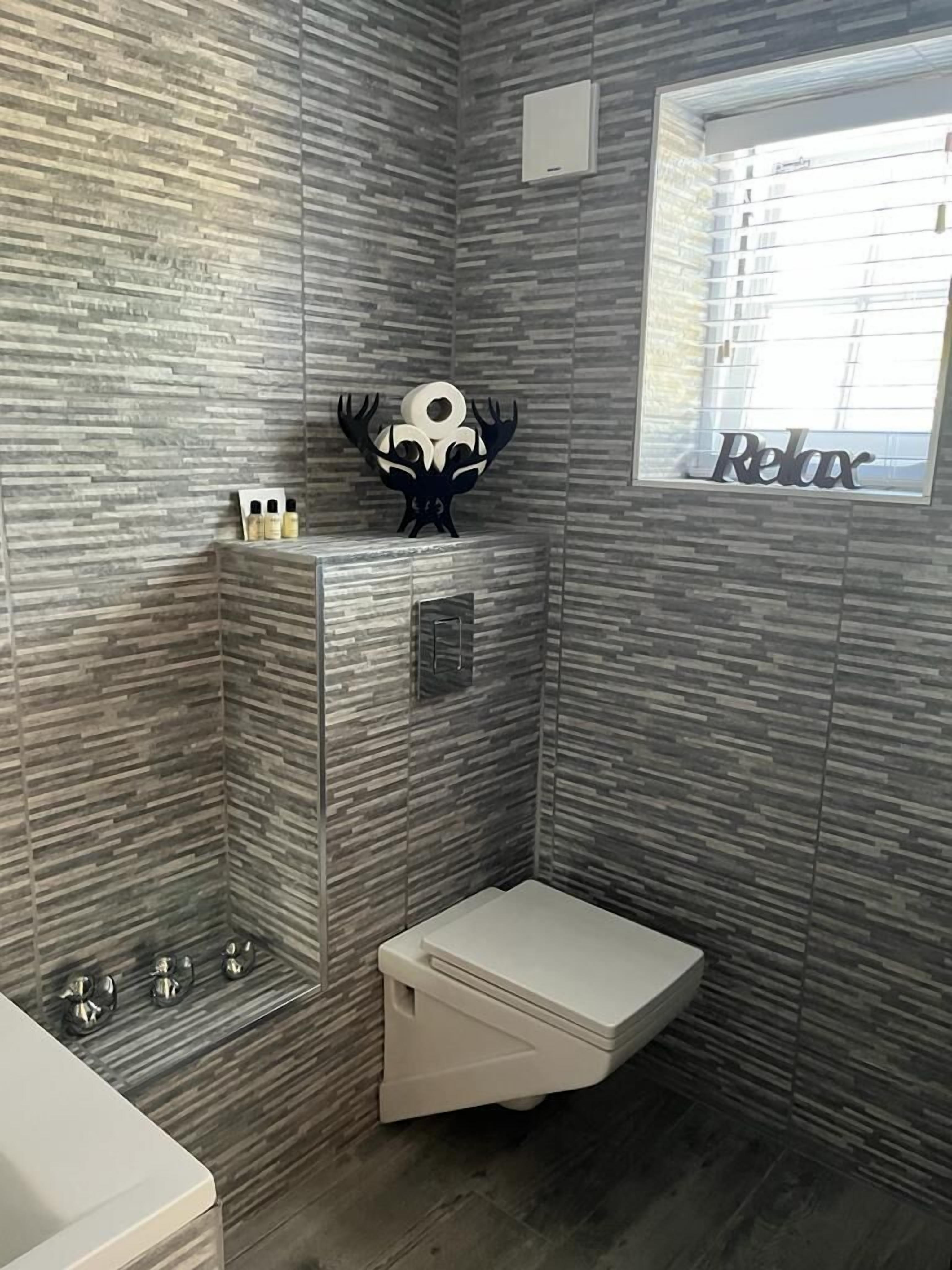 A bathroom with a shower, a toilet, and a vanity. There is a decorative piece on the wall and a window with the word "Relax" on it.