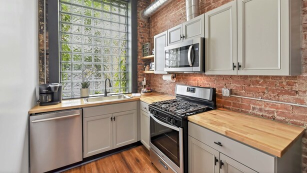 A kitchen with a brick wall, stainless steel appliances, and a window with a view of greenery. - A Cleveland Modern and Historic Apartment (Cleveland)