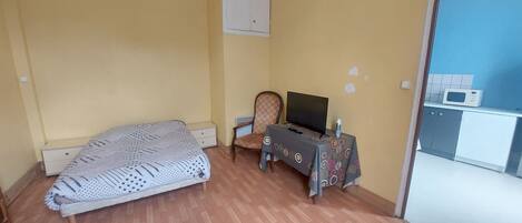 Een slaapkamer met een bed, een stoel, een tafel met een televisie en een kitchenette.
