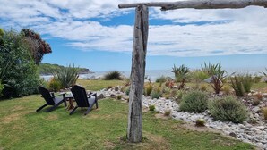 Un área de estar al aire libre con dos sillas y una mesa, rodeada por un jardín con diversas plantas y vistas al mar.