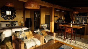 Una habitación acogedora con una cama, dos sofás de mimbre con mantas suaves, una mesa de comedor con sillas, una zona de cocina y un espejo grande en la pared.