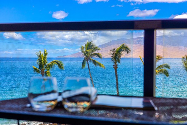 A view from a window overlooking a beach with palm trees and a mountain in the background.