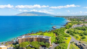 A coastal hotel with a view of the ocean and a mountain in the distance.