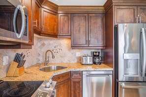 A kitchen with wooden cabinets, a stainless steel refrigerator, a coffee maker, a toaster, and a sink with a modern faucet.