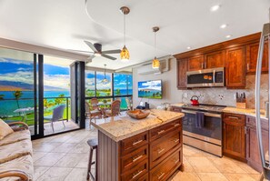 A modern kitchen with a large island, stainless steel appliances, and a view of the ocean.