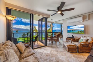 A spacious balcony with a view of the ocean, furnished with wicker furniture and a ceiling fan.