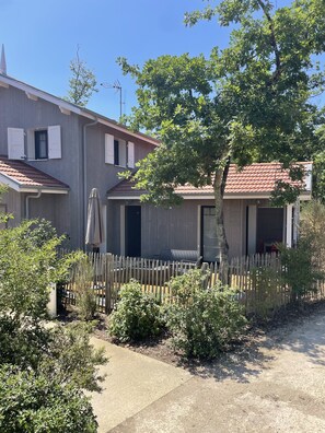 A two-story building with a wooden fence, a tree, and a concrete path.