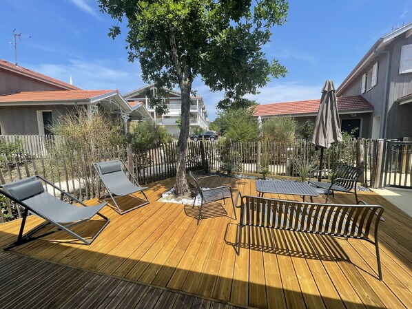 A wooden deck with lounge chairs and a table, surrounded by a wooden fence and trees.
