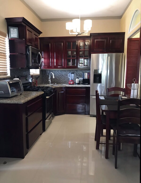 A modern kitchen with dark wood cabinets, stainless steel appliances, and a granite countertop. - The Ansen Place (Belmopan)