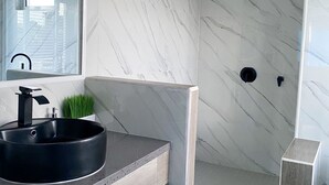 A modern bathroom with a marble wall, a black sink, and a shower area. - The Ansen Place (Belmopan)