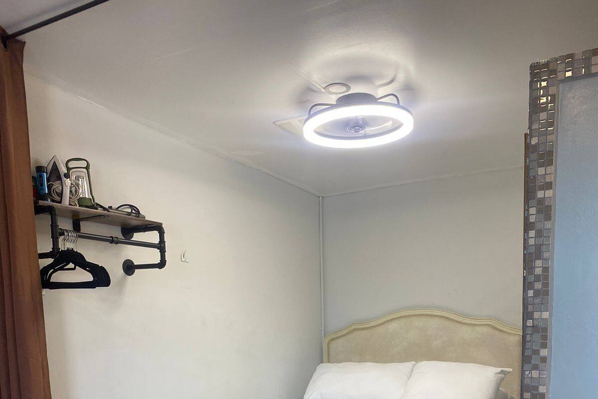 A bedroom with a bed, a bench, a shelf with hangers, and a ceiling light.