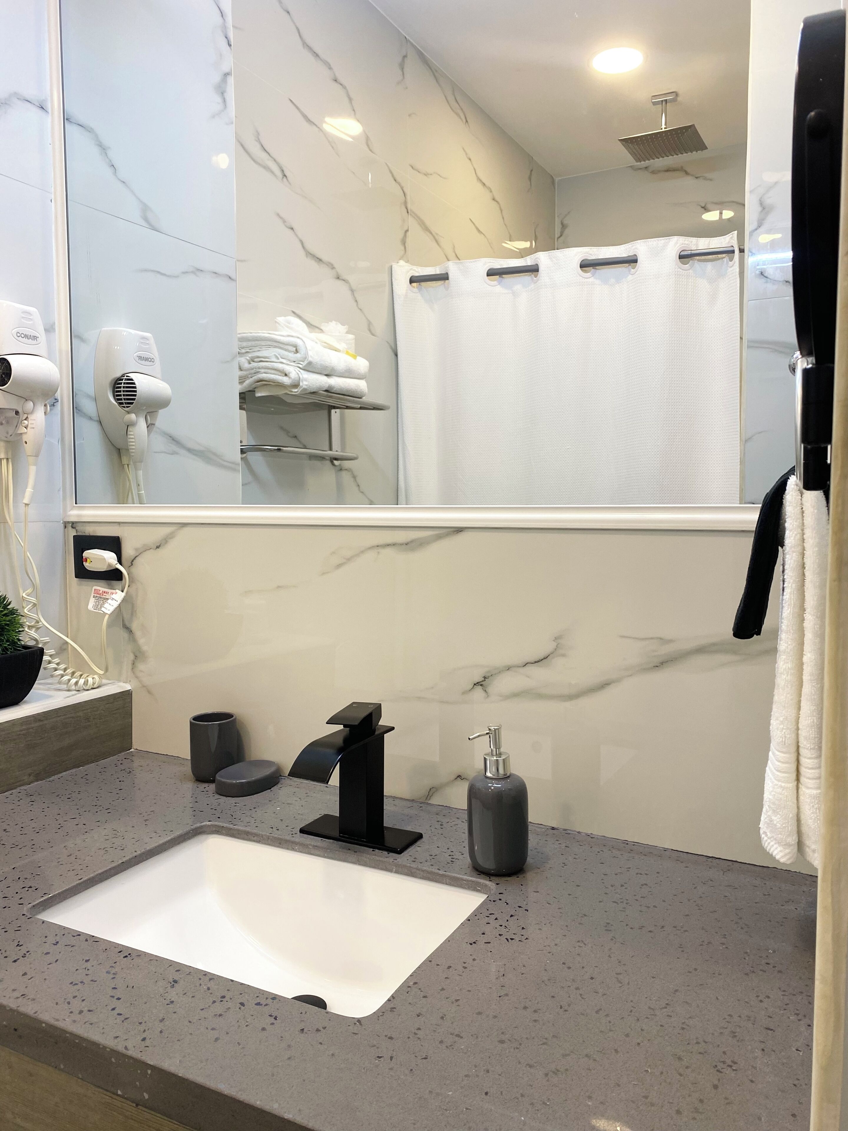 A modern bathroom with a marble vanity, a sink, a towel rack, a hairdryer, and a shower curtain.