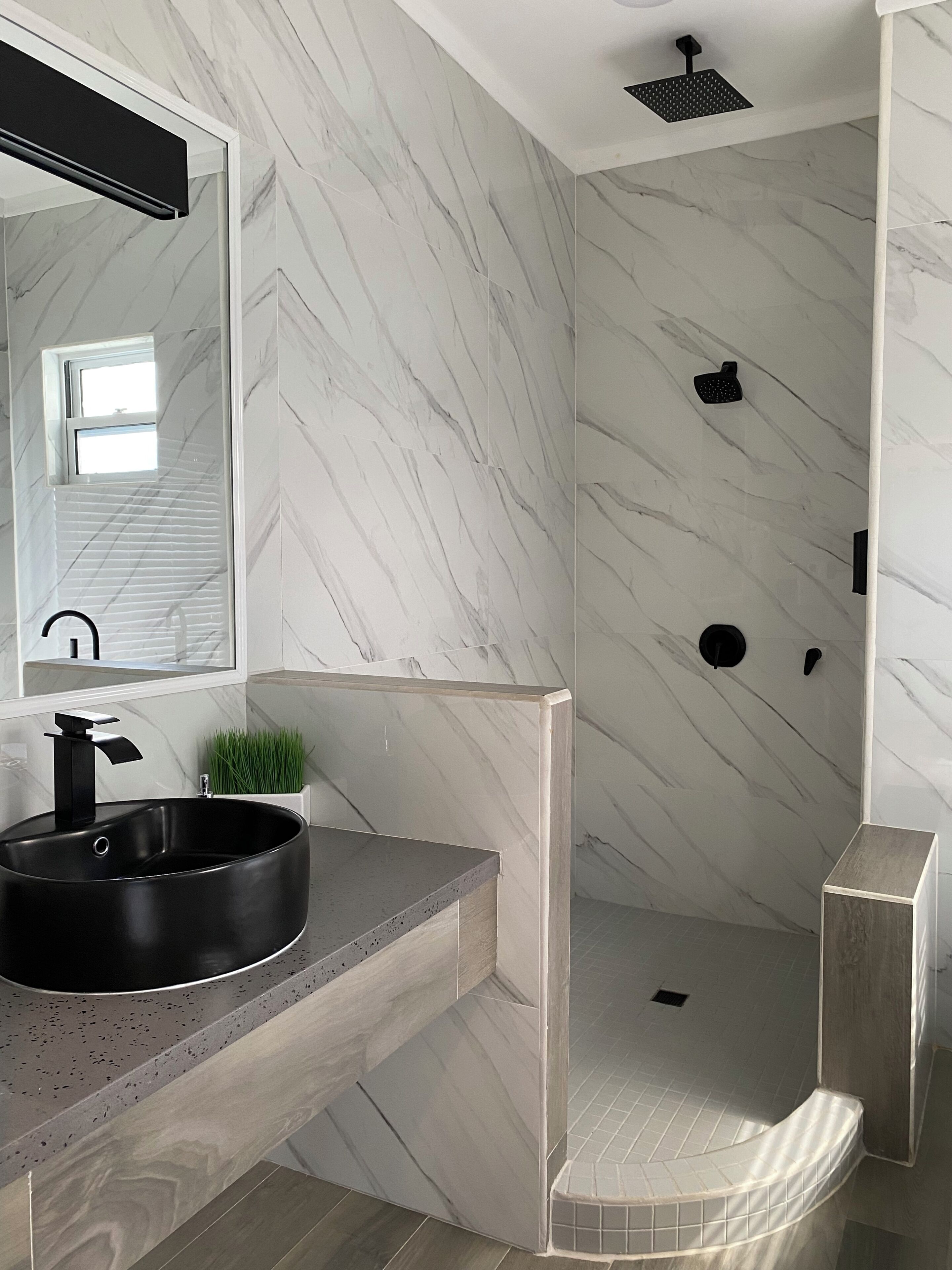 Un baño moderno con pared de mármol, un lavabo negro y zona de ducha.
