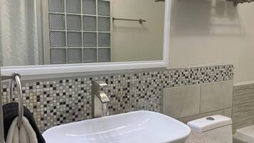 Ein Badezimmer mit weißem Waschbecken, einer Duschkabine aus Glas und einer gefliesten Rückwand.